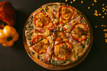 top view Traditional Italian pizza with bacon, paprika, caramelized onions and corn on a black rustic wood background. Top view of hot pizza.