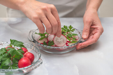 Fresh sliced radish with fresh green parsley close up on glass plate on light grey background. Woman serving vegetable salad