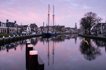 Sailboat in the deserted harbor of Lemmer in winter with sunset with Reformed Church in Friesland,...