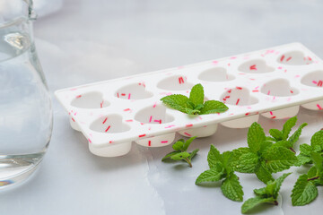Heart shaped ice molds and fresh green mint leaves close up on light marble background. Drinks with frozen mint leaves recipe