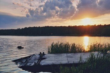 evening summer landscape, the setting sun is reflected on the surface of the water of a small reservoir, on the shore of the reservoir there is a forest, an iron structure lies in the high green grass