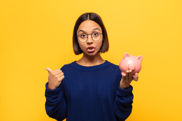 young latin woman looking astonished in disbelief, pointing at object on the side and saying wow,...