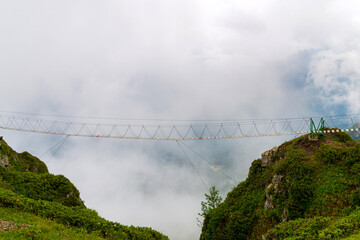 Hanging bridge over chasm in fog. Rope bridge between peaks in cloud