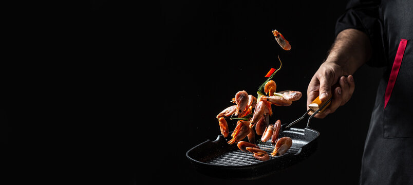 Chef hands cooking shrimps or prawn in pan on black background. banner, menu, recipe, place for text