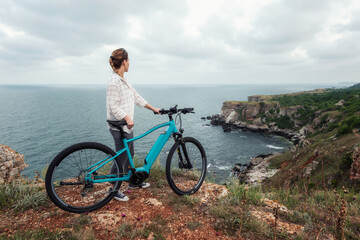 Woman with a bike in the nature / Morning view of a woman with an electric bike enjoys the view of the rocky Black Sea coast.