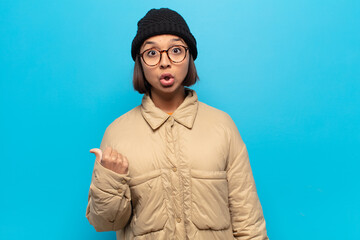 young latin woman looking astonished in disbelief, pointing at object on the side and saying wow,...