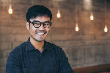 Fototapeta premium asian man portrait young male wear eye glasses smiling cheerful look thinking position with perfect clean skin posing on cafe background.fashion people life style concept