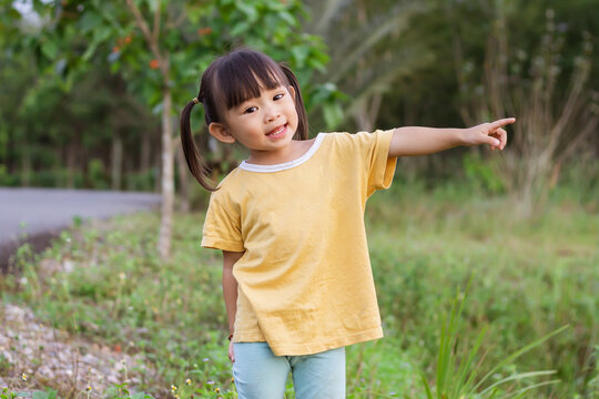Portrait image of 2-3 years old of baby. Happy Asian child girl pointing her finger of the right hand. She playing at the playground or the park.