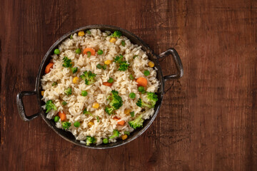Vegan rice with vegetables, shot from above in a frying pan on a rustic wooden background with copyspace