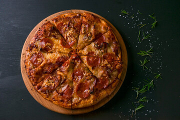 Tasty pepperoni pizza and cooking ingredients tomatoes basil on black wood background. Top view of hot pepperoni pizza. With copy space for text. Flat lay. Banner