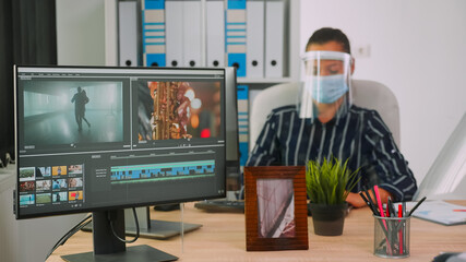 Videographers with protection masks working at video project creating content, team of bloggers sitting in new normal office studio. Freelancers editing video durig global pandemic