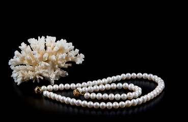 Natural pearl necklace, bracelet and branch of sea white coral isolated on black background. Copyspace  for text