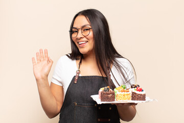 young latin woman smiling happily and cheerfully, waving hand, welcoming and greeting you, or saying goodbye