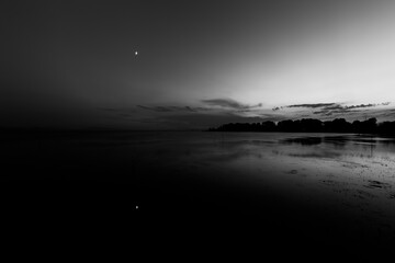 Moon above a lake with its reflection on the Trasimeno lake surface at dusk