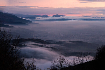 Naklejka na ściany i meble Mist and fog between valley and layers of mountains and hills at dusk, in Umbria (Italy), with city lights underneath