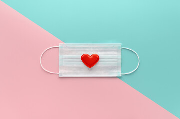 New normal Valentine's Day concept. Medical face mask decorated with red heart on pastel pink and...
