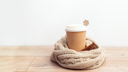 paper cup of coffee wrapped in a santa hat on a white and wooden christmas background.