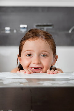 Cute young girl with toothless smile peeking over bathtub