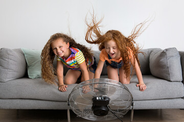 Two funny young girls on couch facing a fan