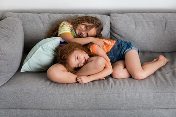 Two happy young girls cuddling on sofa