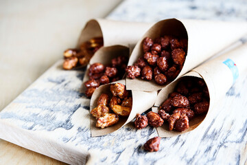 Caramelized sugared peanuts in paper envelope bags on wooden background. Selective focus