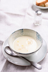 Cauliflower and Potato Cream Soup served with herbs and pepper on white linen striped tablecloth. Selective focus