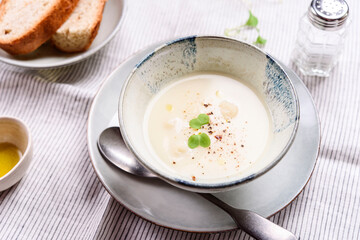 Cauliflower and Potato Cream Soup served with herbs and pepper on white linen striped tablecloth. Selective focus