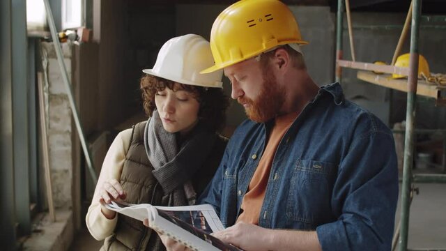 Chest up shot of male and female architects in hardhats having discussion and then posing together for camera and smiling while working at constriction site