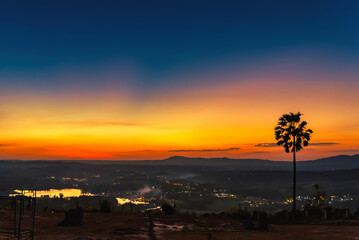 Silhouette palm tree on sunrise with colorful twilight sky on the mountain.