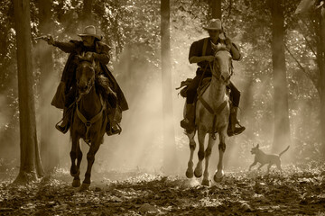 Vintage photo of two cowboy men sitting on horseback and shooting handgun pistols.