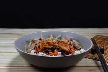 Fried and stirred pork with sliced onion in local style serving with cooked rice and kimchi (Korea spicy pickled mixed vegetable) on the plate.