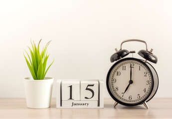 January 15 on a wooden calendar, next to a retro alarm clock and a succulent in a mini pot on a light table.One day in January.Winter day.A copy of the space.Workplace.