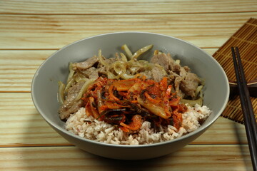 Fried and stirred pork with sliced onion in local style serving with cooked rice and kimchi (Korea spicy pickled mixed vegetable) on the plate.