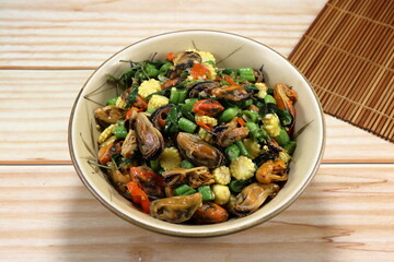 Fried and stirred spicy mussel meat with cutting baby corn, chilly and basil in the bowl. Famous traditional seafood menu in Asia restaurant. 