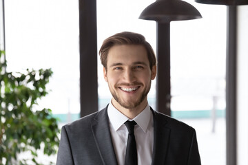Profile picture of smiling young Caucasian businessman in formal suit posing in office. Close up...