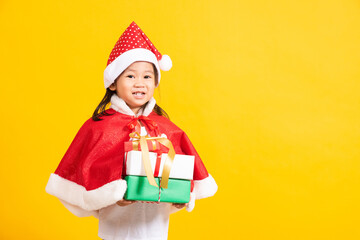 Asian little cute girl smile and excited, Kid dressed in red Santa Claus hat hold gift box on hands concept of holiday Christmas Xmas day or Happy new year, studio shot isolated on yellow background