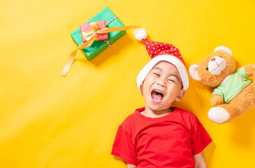 Asian little cute child boy smile, Top view of a kid dressed in red Santa Claus hat the concept of holiday Christmas Xmas day or Happy new year, isolated lying on yellow background