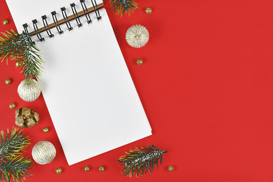White empty notebook surrounded by Christmas decoration in corner of red background with empty copy space