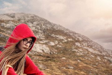 Young teenager girl in red hoodie, Diamond hill in the background. Travel and hike concept. The model has long hairs and wears glasses. Connemara, county Galway, Ireland