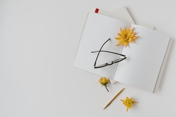 Minimalist home office desk workspace. Blank paper sheet notebook, glasses, yellow flower bud, stationery. Flat lay, top view. Copy space mockup template for blog, social media, website.
