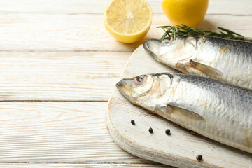 Board with fresh herring fish and spices on white wooden background