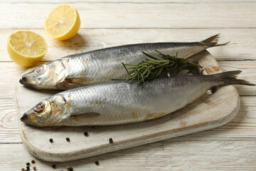Board with fresh herring fish on white wooden background
