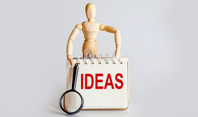 Wooden man shows with a hand to white notepad with text IDEAS