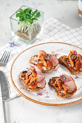 Open sandwiches on rye bread with pickled mushrooms chanterelles and ham on a white plate