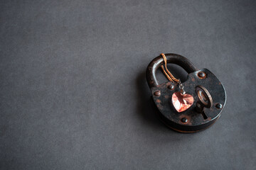 Key to heart concept. Red heart shaped pendant, necklace locked on old rusty lock with key in keyhole on grey grunge background with blank space for text. Copy space. Close up. Top view