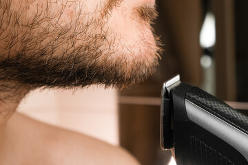 Front view on the man shaving his cheek using electric razor 
