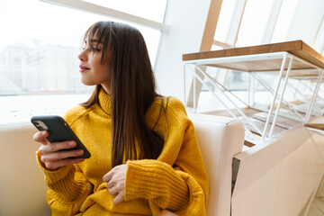Charming happy girl using mobile phone and sitting on couch