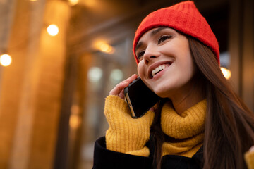 Charming happy girl talking on mobile phone while standing at city