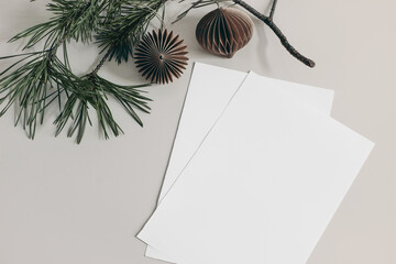 Christmas still life. Blank paper sheets mockups and green pine tree branch on beige table...