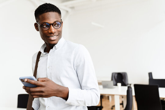 Afro american pleased man in eyeglasses smiling and using mobile phone